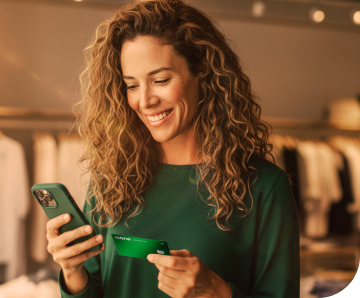 A empreendedora em sua loja de roupas, com linhas de costuras atrás está segurando um celular para enviar o link de pagamento aos seus clientes através do Messenger do Facebook, Whatsapp e Instagram.