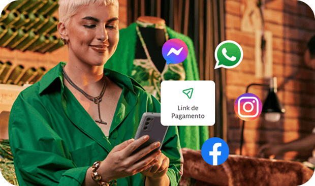 A empreendedora em sua loja de roupas, com linhas de costuras atrás está segurando um celular para enviar o link de pagamento aos seus clientes através do Messenger do Facebook, Whatsapp e Instagram.