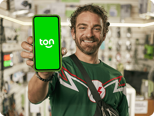 Homem com camisa verde sorrindo e mostrando o celular com o logo do Ton em sua mão