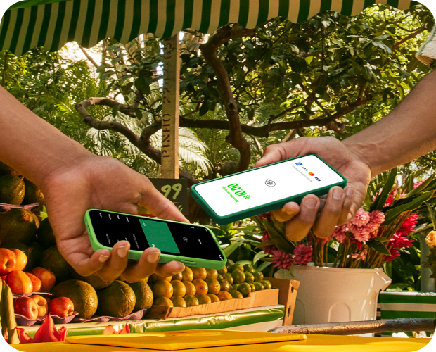 Empreendedora está utilizando o seu celular como Máquina de Cartão e o cliente está passando o seu cartão por aproximação. Ao lado estão alguns cupcakes e utensílios de cozinha.